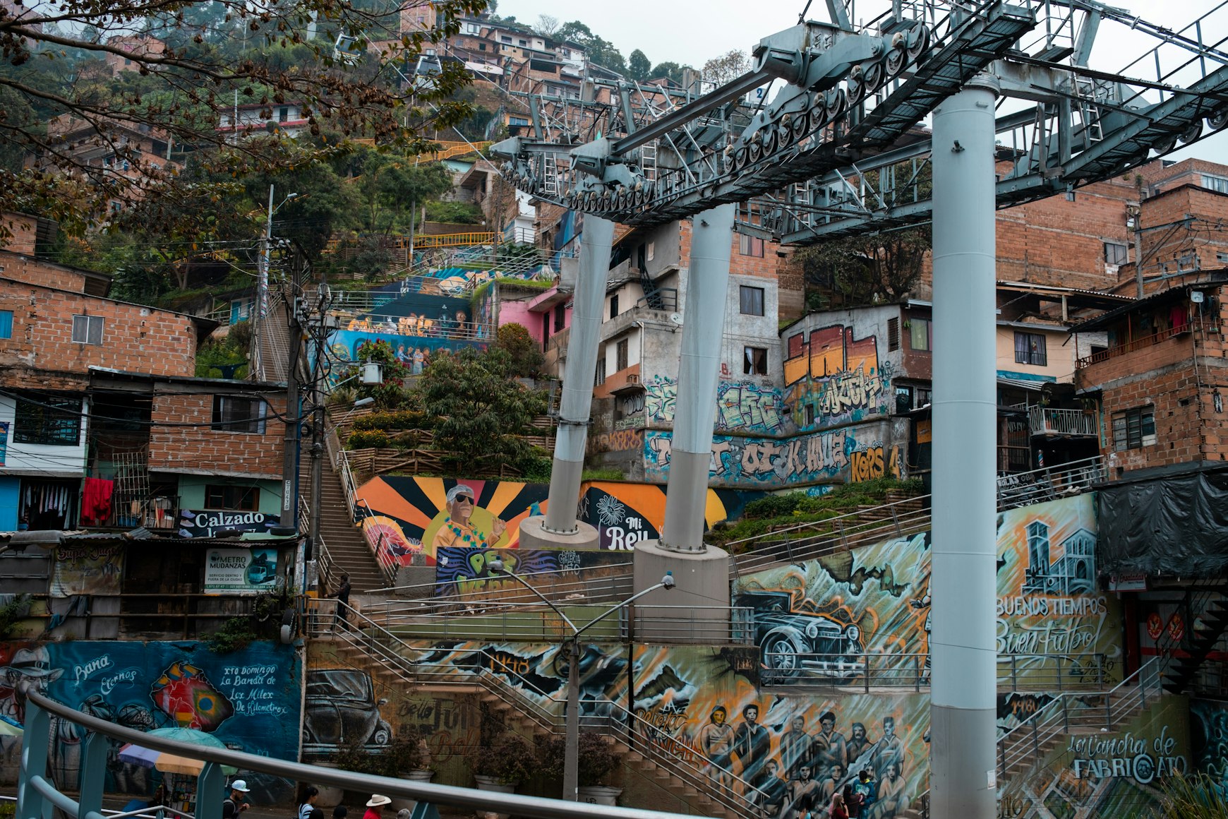 Murals, stairways and red-brick hillside homes beneath the cable-car infrastructure in Medellín, Colombia.
