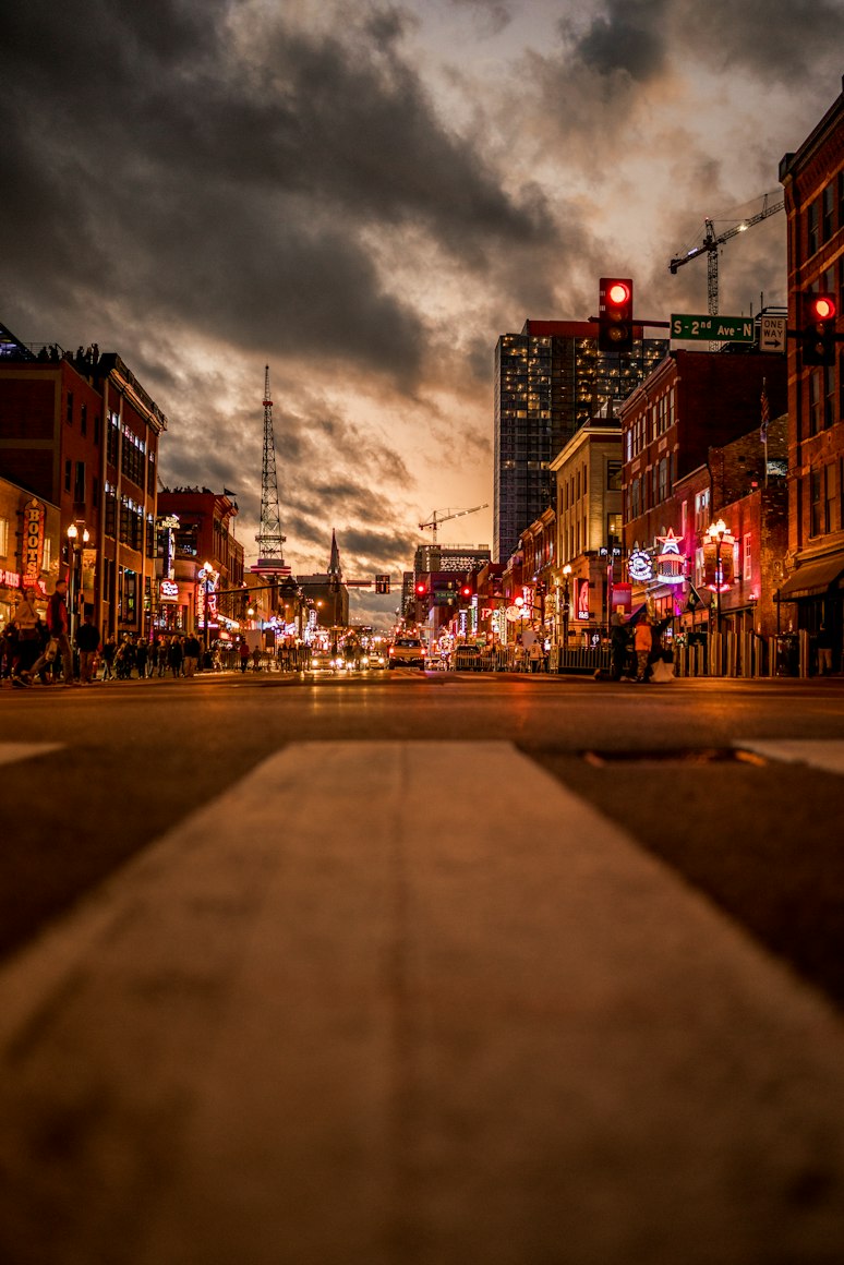 Broadway in Nashville at dusk, with illuminated honky-tonks and downtown buildings.