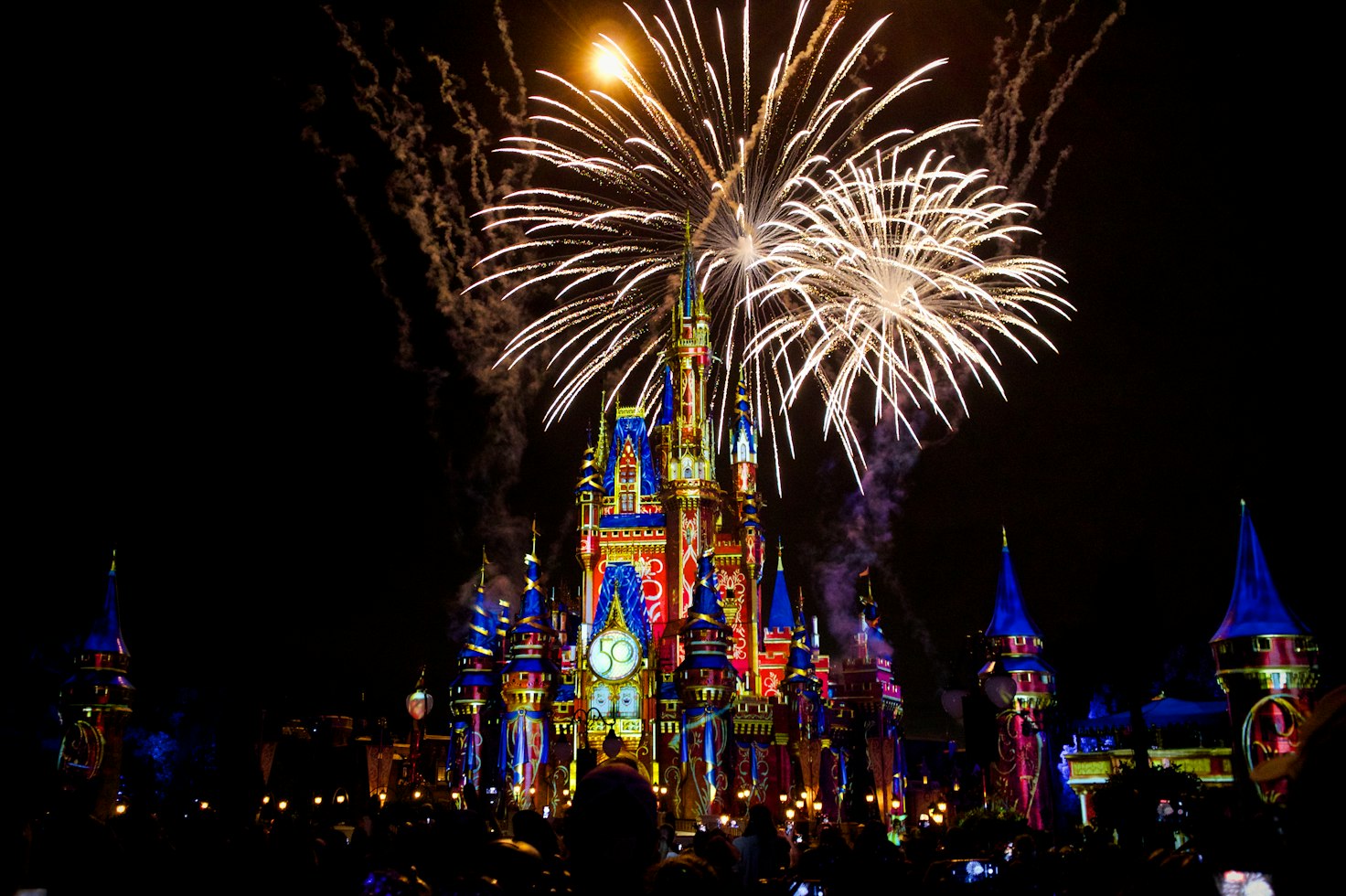 Cinderella Castle at Walt Disney World illuminated beneath fireworks at night.